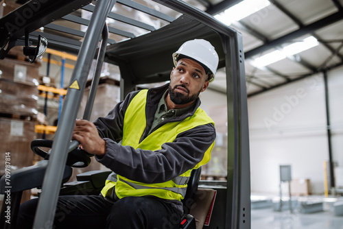 Portrait of warehouse worker driving forklift. Warehouse worker preparing products for shipmennt, delivery, checking stock in warehouse.