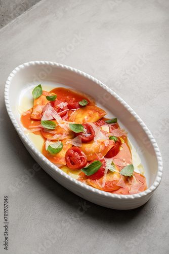 Delicious Italian ravioli pasta with tomato sauce, parmesan cheese and fresh basil leaves on a gray background