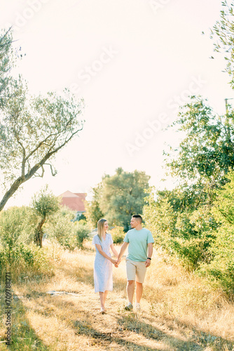 Man and woman walk on dry grass in a sunny garden holding hands © Nadtochiy