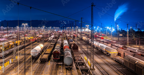 Panoramic view of large shunting yard and freight station in Hagen Germany on a cold winters night. Brightly illuminated colorful infrastructure with trains, cars and wagons an many parallel tracks.