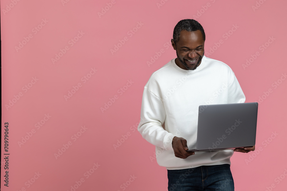 Joyful black man wearing white sweatshirt using laptop copy space Joyful black man wearing white sweatshirt using laptop copy space