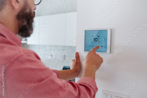 Man using smart thermostat, adjusting, lowering heating temperature at home. Concept of sustainable, efficient, and smart technology in home heating and thermostats.