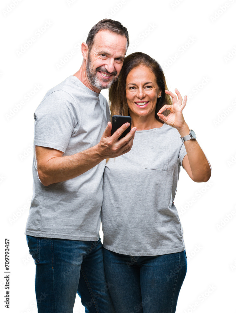 Middle age hispanic couple texting message on smartphone ver isolated background doing ok sign with fingers, excellent symbol Middle age hispanic couple texting message on smartphone ver isolated background doing ok sign with fingers, excellent symbol