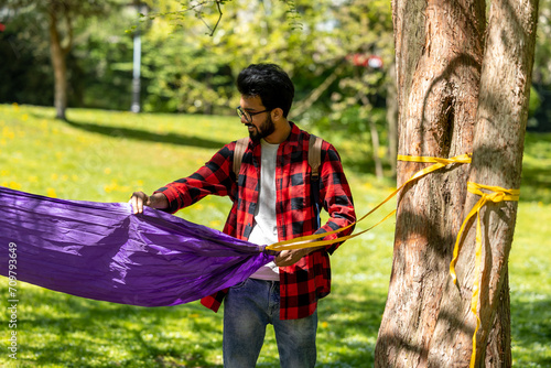 Young hindu man fixing hammock to the tree in the park