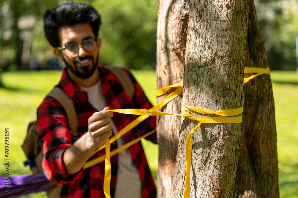 Man in checkered shirt tying ropes to the tree and adjusting hammock