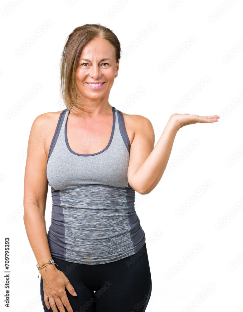 Fototapeta premium Beautiful middle age woman wearing sport clothes over isolated background smiling cheerful presenting and pointing with palm of hand looking at the camera.
