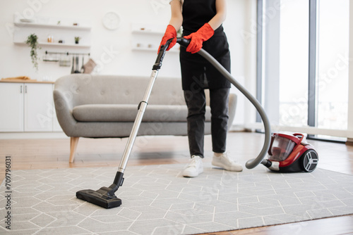 Cropped view of hands holding vacuum cleaner of Caucasian female cleaning service worker vacuums rug in living room kitchen. Concept of cleaning and disinfection in modern apartments.