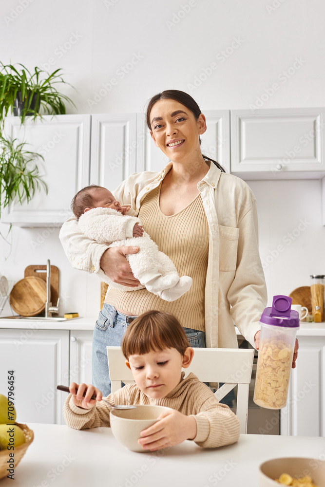 jolly beautiful mother enjoying breakfast with her toddler and newborn sons, modern parenting