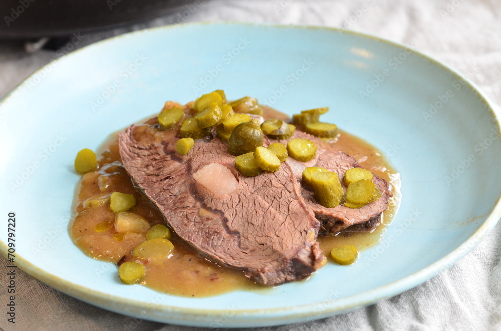 beef stew with pickled green cucumber and serving on a blue plate, czech food beef stew with pickled green cucumber and serving on a blue plate, czech food