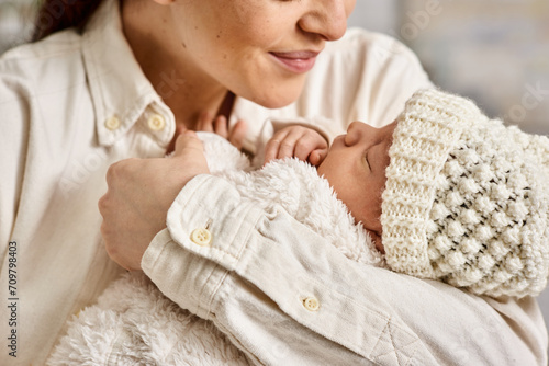 good looking joyful mother in homewear holding lovingly her newborn baby boy, modern parenting