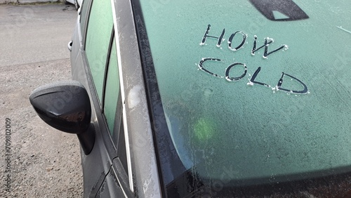 Che freddo scritto su un'auto con il parabrezza coperto di ghiaccio. photo