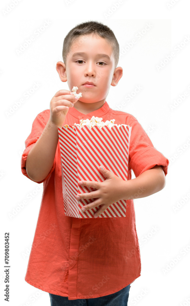 Dark haired little child eating popcorn with a confident expression on smart face thinking serious Dark haired little child eating popcorn with a confident expression on smart face thinking serious