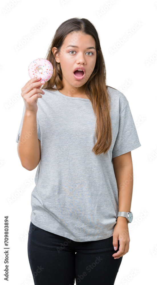 Young beautiful woman eating pink donut over isolated background scared in shock with a surprise face, afraid and excited with fear expression Young beautiful woman eating pink donut over isolated background scared in shock with a surprise face, afraid and excited with fear expression