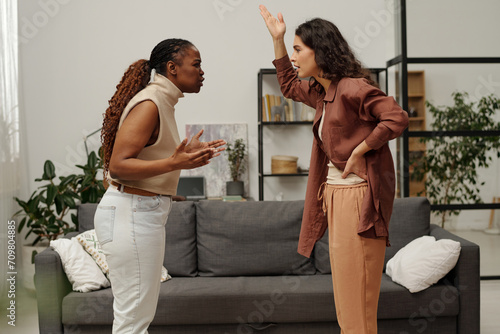 Obraz na plátně Side view of two young angry girlfriends shouting at one another and gesturing b