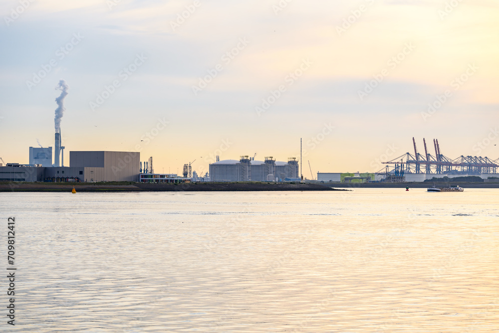 Industrial buildings, fuel storage tanks and gantry cranes at a major seaport at sunset in summer