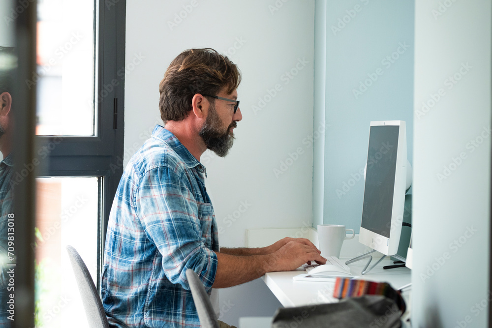 Caucasian freelance people man sitting at the desk typing on desktop computer for online job internet connected lifestyle - hipster adult male working at home or office cowork space alone