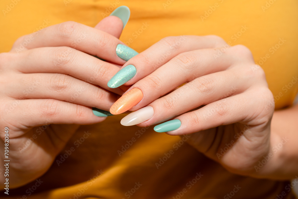 Female hands with glitter nail polish. Green and orange nail design with two shades. Women hands with sparkle colored manicure.