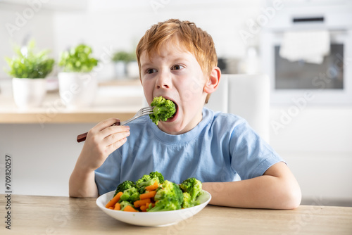 A little boy is having lunch and eating broccoli