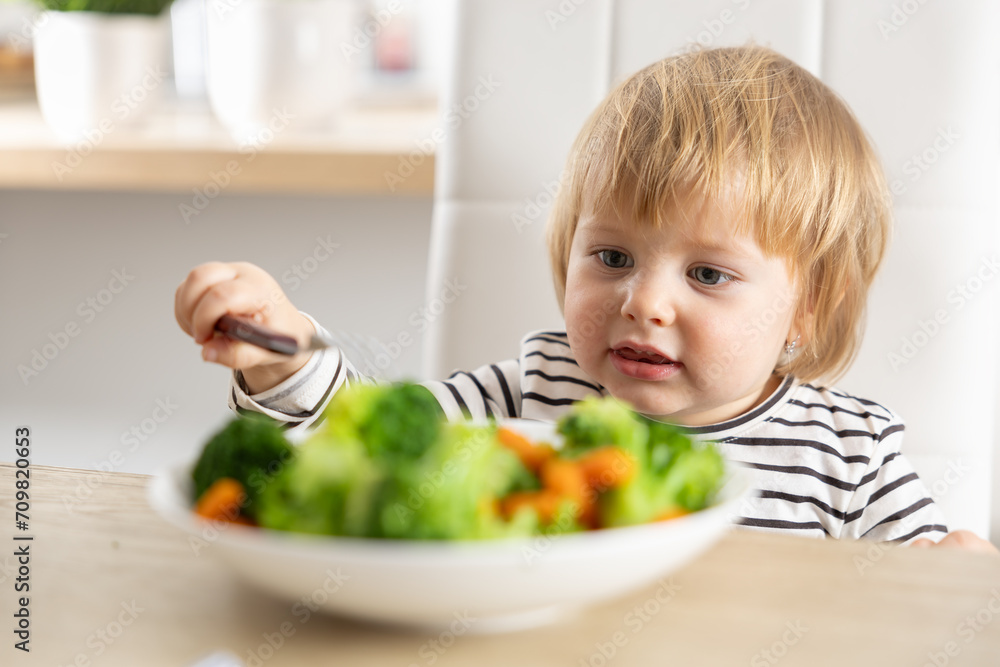 Cute little girl is eating broccoli and carrot vegetables with a fork Cute little girl is eating broccoli and carrot vegetables with a fork