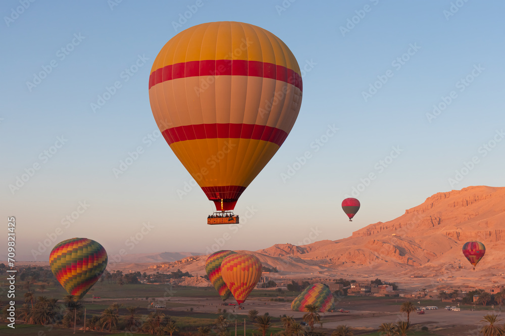 Fototapeta premium Hot air balloon flying over Hatshepsut Temple at sunrise in Valley of the Kings and red cliffs western bank of Nile river - Luxor- Egypt