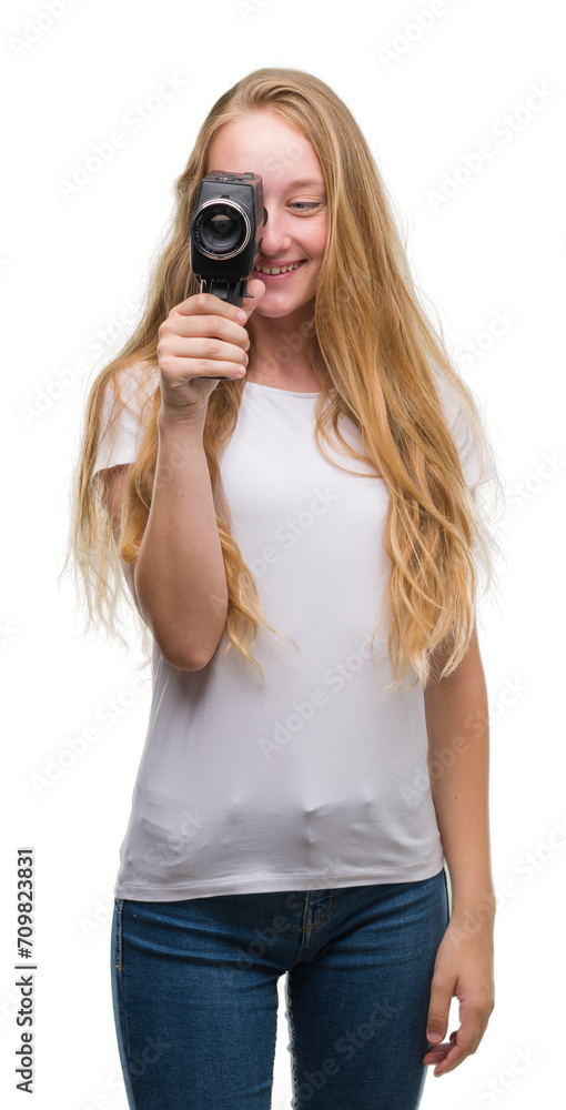 Blonde woman teenager filming holding super 8 video camera with a happy face standing and smiling with a confident smile showing teeth Blonde woman teenager filming holding super 8 video camera with a happy face standing and smiling with a confident smile showing teeth