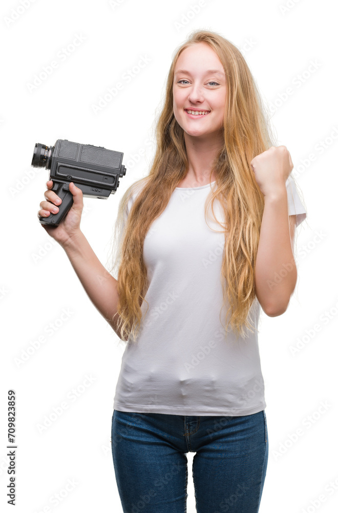 Blonde woman teenager filming holding super 8 video camera screaming proud and celebrating victory and success very excited, cheering emotion Blonde woman teenager filming holding super 8 video camera screaming proud and celebrating victory and success very excited, cheering emotion