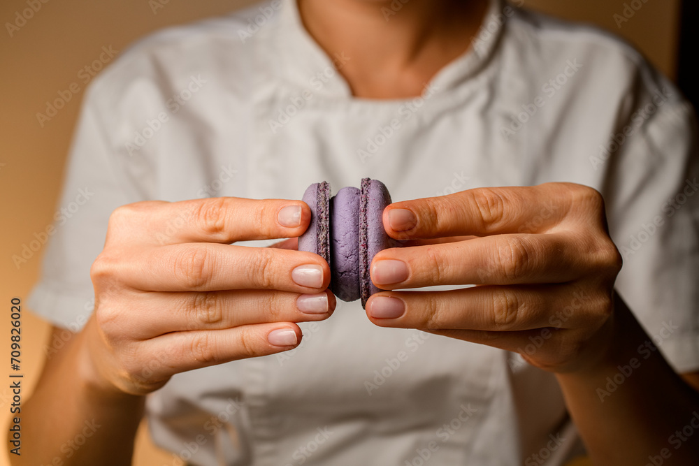 Fototapeta premium Close-up of confectioner's female hands holding together halves of macaroons