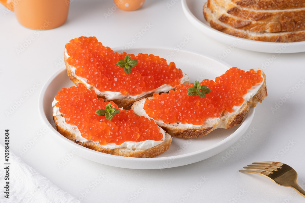 Three sandwiches with red caviar on a plate. A delicious appetizer of trout caviar on a slice of bread with cream cheese. Salted salmon caviar for fish delicacy concept