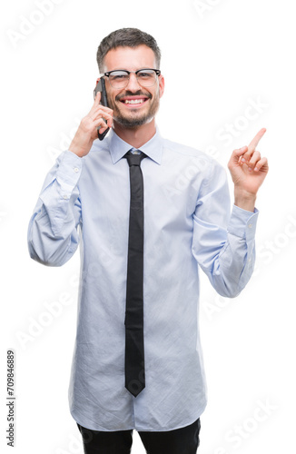 Young business adult man talking on the phone very happy pointing with hand and finger to the side