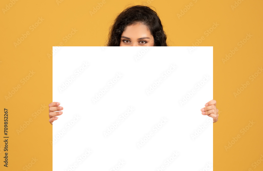 Curious woman peering over a blank white board with just her eyes and forehead showing Curious woman peering over a blank white board with just her eyes and forehead showing