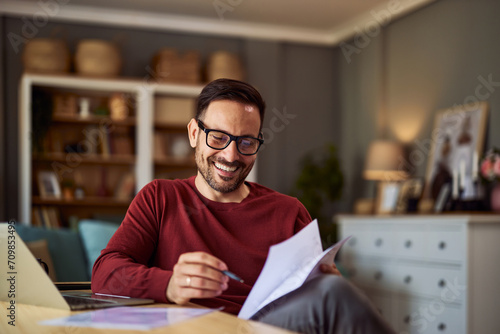 A cheerful remote accountant with glasses reading male financial reports while working from home. photo