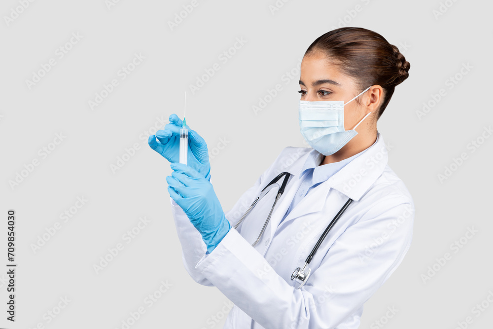Concentrated european doctor in a lab coat and protective mask, carefully examining a syringe Concentrated european doctor in a lab coat and protective mask, carefully examining a syringe