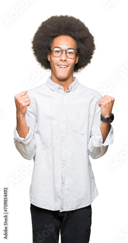 Young african american man with afro hair wearing glasses celebrating surprised and amazed for success with arms raised and open eyes. Winner concept.