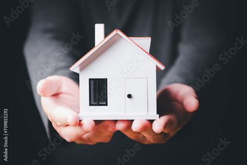 Close-up of hands holding a small white house model, symbolizing home ownership, insurance, or real estate concept.