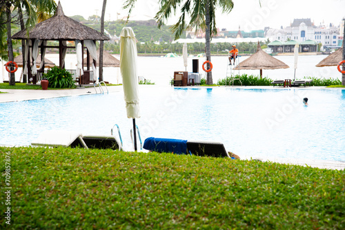 Unidentified Asian tourist enjoy swimming at ocean view swimming pool with lifebuoy, lounge chairs, coconut palm trees and mountain range in background at upscale resort hotel in Nha Trang