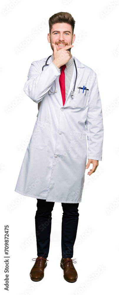 Young handsome doctor man wearing medical coat looking confident at the camera with smile with crossed arms and hand raised on chin. Thinking positive. Young handsome doctor man wearing medical coat looking confident at the camera with smile with crossed arms and hand raised on chin. Thinking positive.