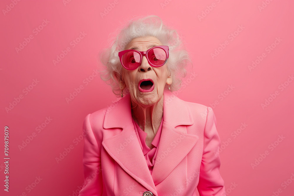 Surprised Mature Woman with Glasses with Big Hair on an Pink Background with Space for Copy. Colorful studio portrait of eccentric elderly granny wearing pink suit with bow tie and sunglasses, Surprised Mature Woman with Glasses with Big Hair on an Pink Background with Space for Copy. Colorful studio portrait of eccentric elderly granny wearing pink suit with bow tie and sunglasses,