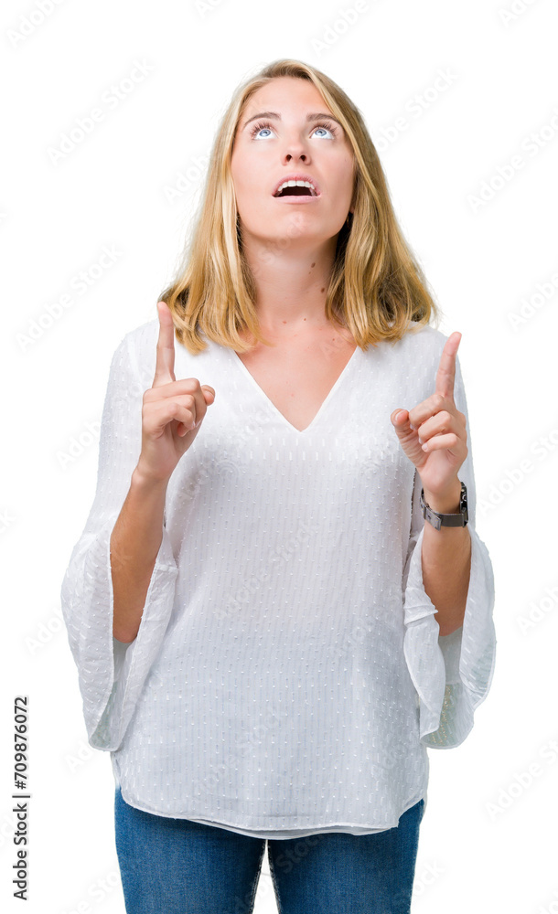 Beautiful young elegant woman over isolated background amazed and surprised looking up and pointing with fingers and raised arms. Beautiful young elegant woman over isolated background amazed and surprised looking up and pointing with fingers and raised arms.