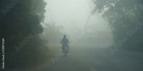 an indian man riding a bike at early morning on foggy road photo