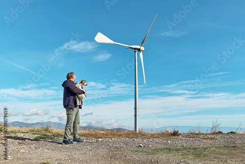 Green energy concept. Man walking with dog near mountain top industrial wind power plant  wind turbine for generating electricity in wind farm or wind park.