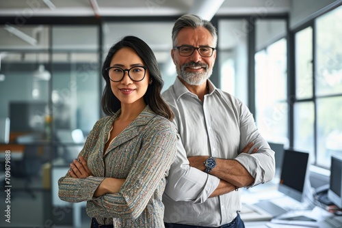 Happy confident professional mature Latin business man and Asian business woman corporate leaders managers standing in office, two diverse colleagues executives team posing arms crossed, Generative AI photo