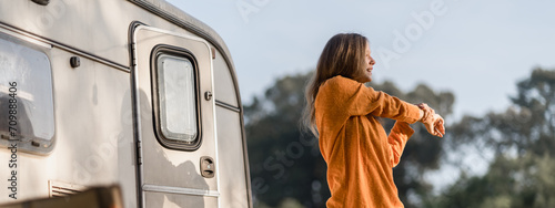 Attractive female feel refreshing and stretching to relax in early morning in front of camper van, motorhome or caravan car trip at park. Camping road trip, freedom vacation, weekend travel or journey photo