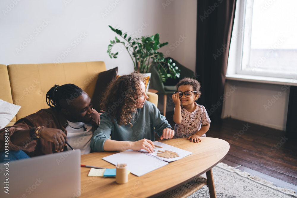 Cheerful multiethnic family sitting by table in living room Cheerful multiethnic family sitting by table in living room