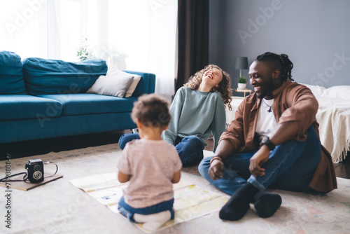 Joyful young diverse parents with little child sitting on floor at home photo