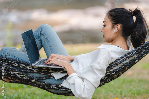 Bilde på lerret A Beautiful Asian, Japanese or Latin female is chilling on cozy hammock and working online with laptop during her vacation or weekend, Carefree and tranquility, wellbeing lifestyle outdoor recreation