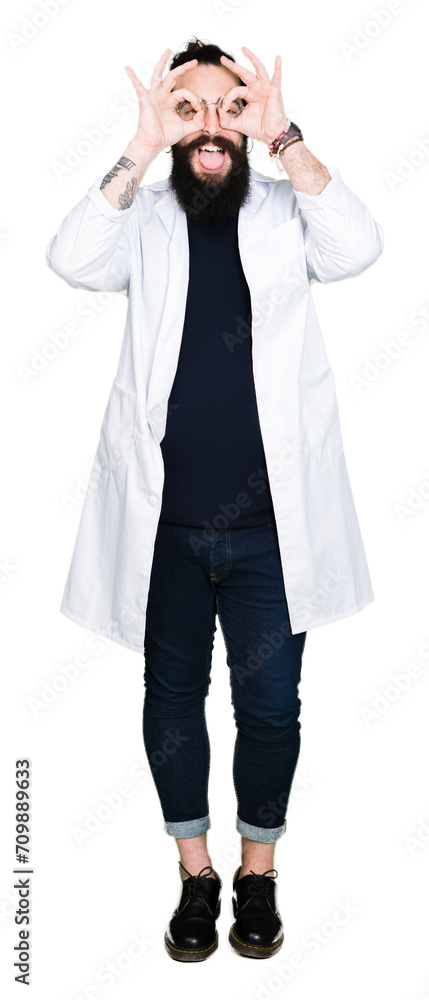 Doctor therapist man with long hair and bear wearing white coat doing ok gesture like binoculars sticking tongue out, eyes looking through fingers. Crazy expression. Doctor therapist man with long hair and bear wearing white coat doing ok gesture like binoculars sticking tongue out, eyes looking through fingers. Crazy expression.