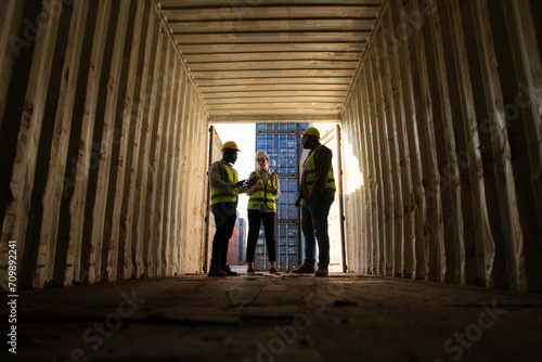 Group of workers in an empty container storage yard, The condition of the old container is being assessed to determine whether it requires maintenance for usage. © Wosunan