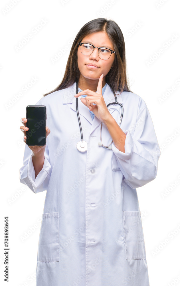 Young asian doctor woman holding smartphone over isolated background serious face thinking about question, very confused idea Young asian doctor woman holding smartphone over isolated background serious face thinking about question, very confused idea