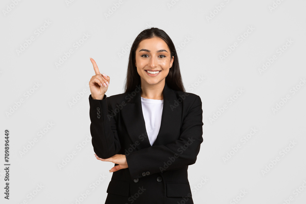 Smiling young caucasian business lady in formal wear pointing finger up at free space, isolated on gray background Smiling young caucasian business lady in formal wear pointing finger up at free space, isolated on gray background