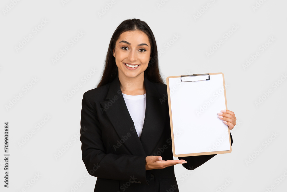 Happy young business lady holding blank clipboard and showing place for design or signing contract Happy young business lady holding blank clipboard and showing place for design or signing contract